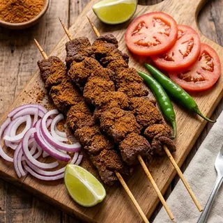Suya skewers on a board with tomato, onion and lime.